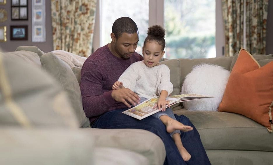 Dad reading a book to his daughter while sitting on a couch