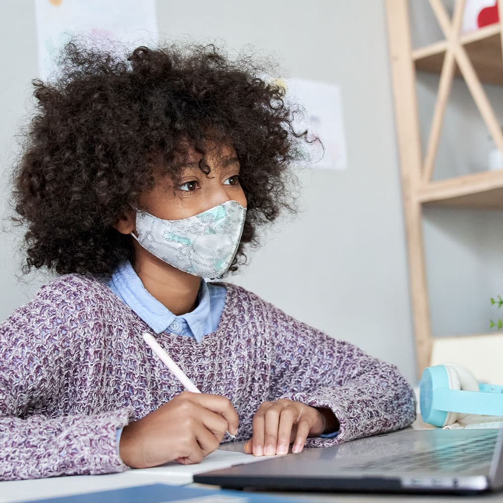 A student with a mask doing virtual school using their laptop.