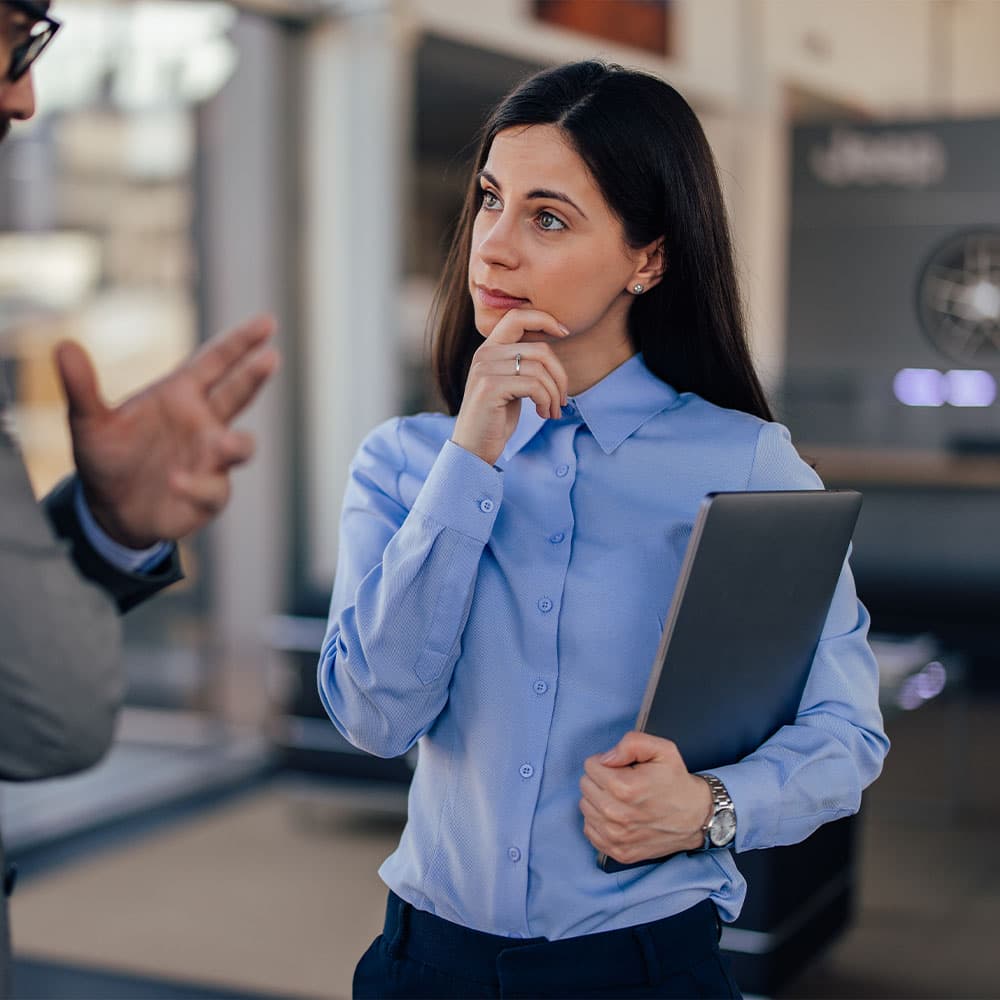 A woman holding a laptop having a discussion with another employee.