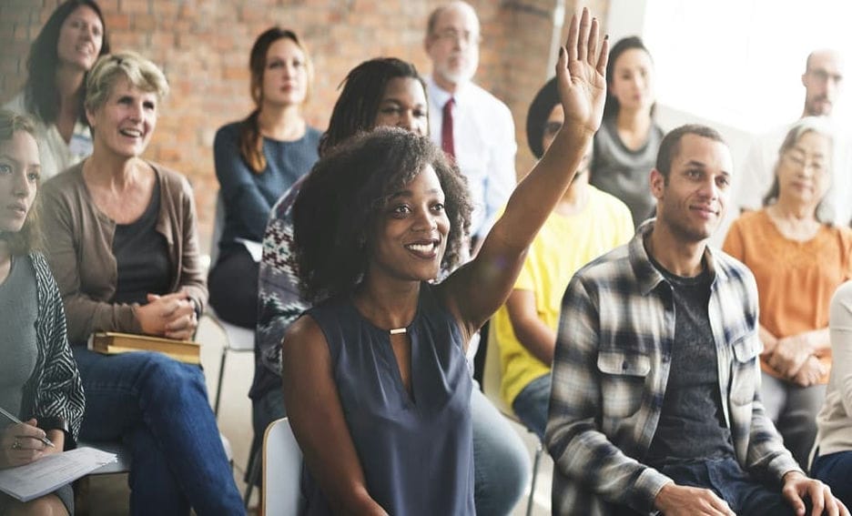 A women raising her hand amidst a group of other parents.