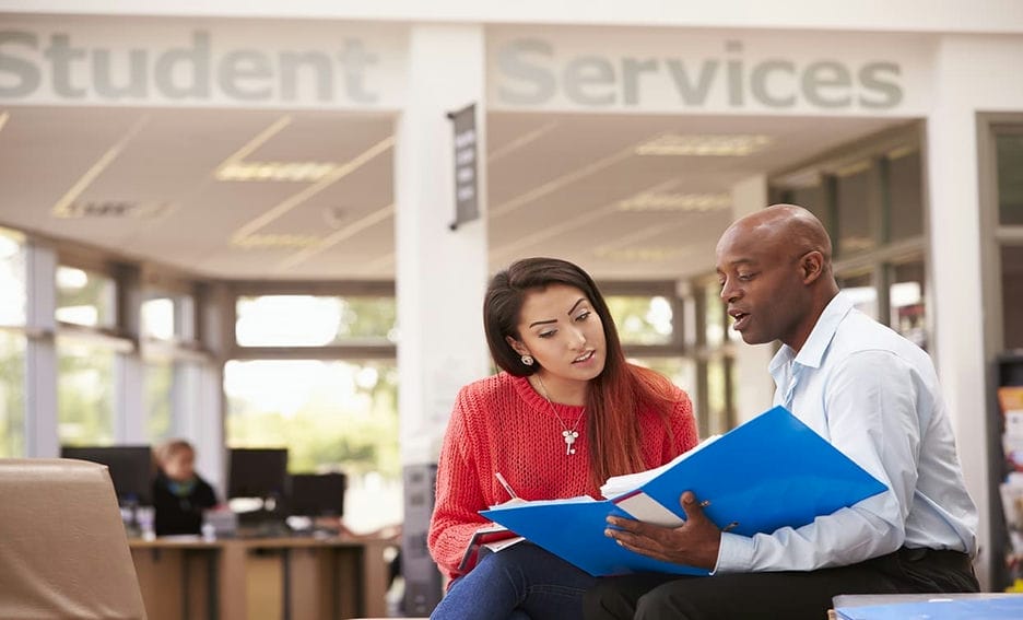 A woman and man discussing something from a binder