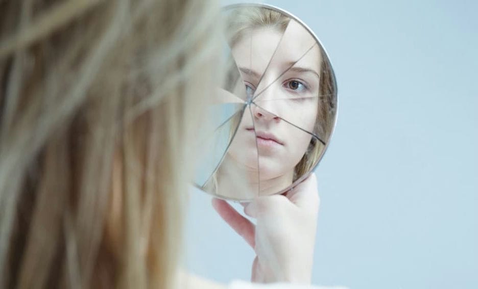 A teenager looking at their reflection in a cracked mirror.