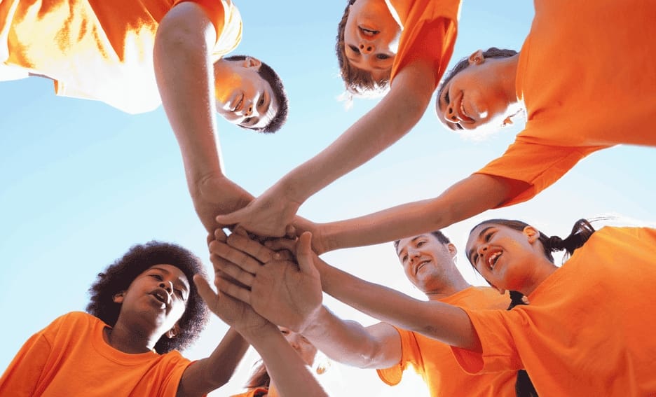 Group of kids wearing orange putting their hands in the center of a circle