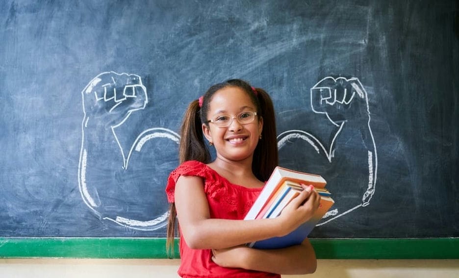 Student standing in front of a chalkboard with illustration of muscles