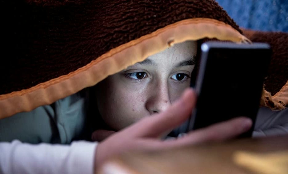 Student in bed on their smartphone under a blanket