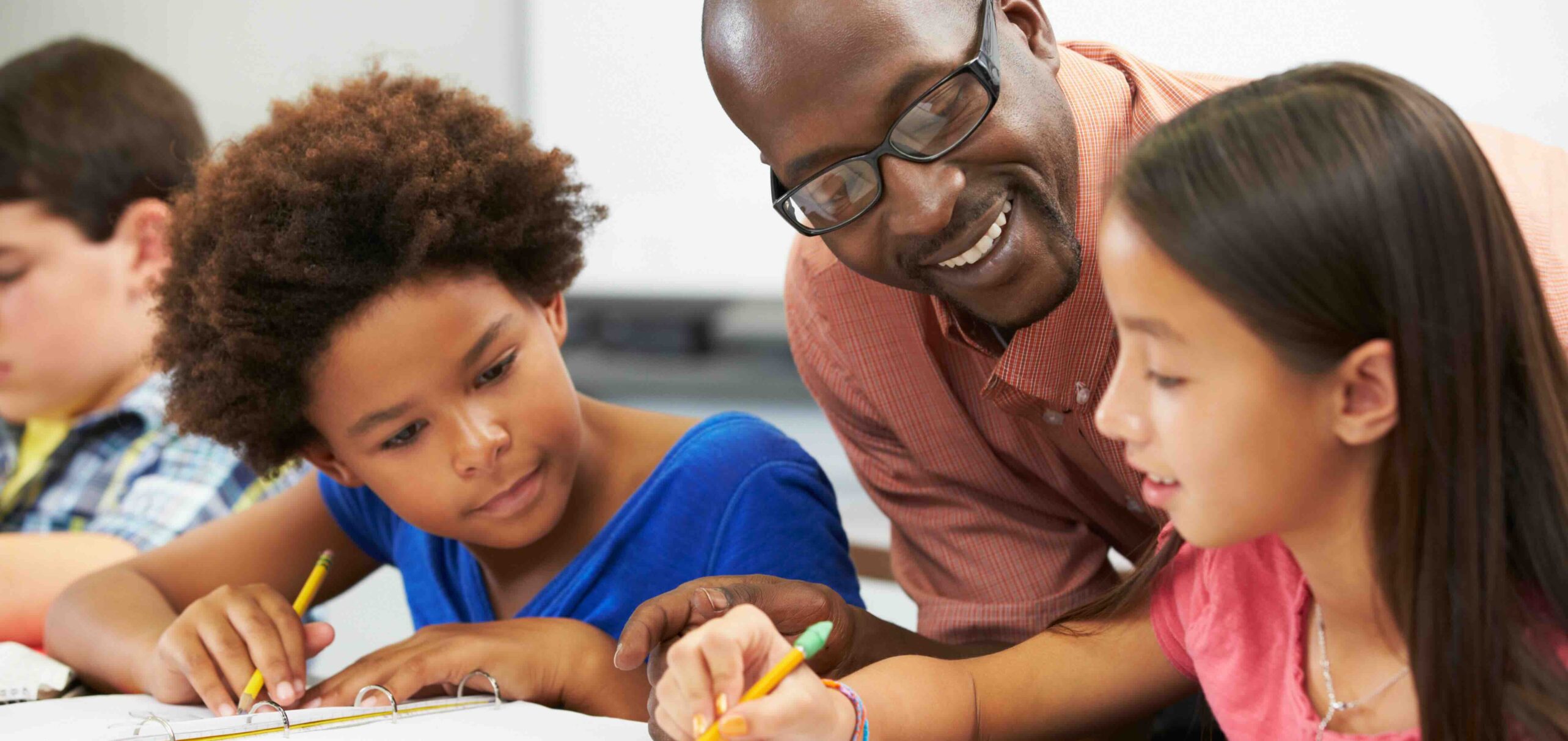 Teacher Helping Pupils Studying At Desks In Classroom